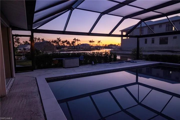 Screened-in swimming pool featuring a tiled waterline, concrete decking, and a covered outdoor area