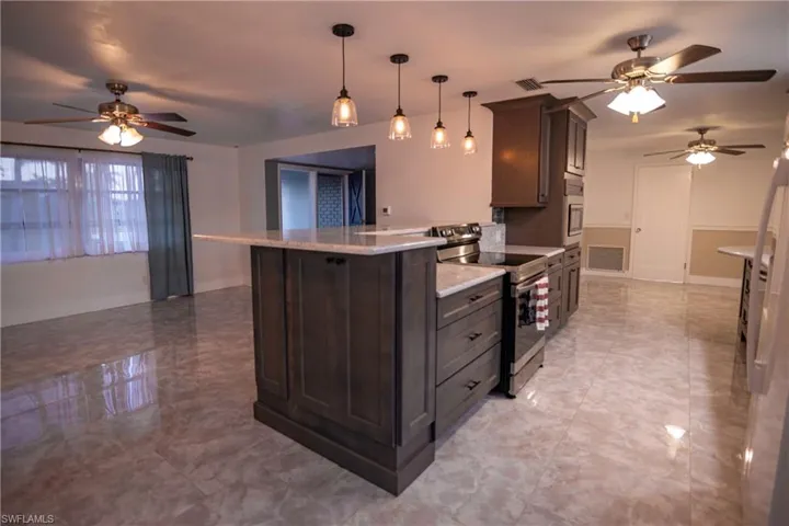Kitchen island featuring an integrated stainless steel range, built-in microwave, and pendant lighting