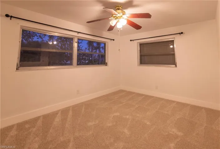 Neutral wall paint with carpet flooring, a ceiling fan with integrated lighting, and two windows with curtain rods