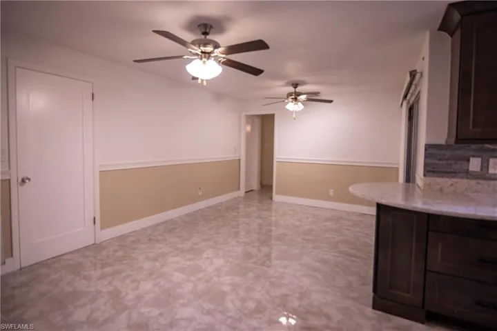 Spacious interior featuring marble-look tile flooring, two-tone wall treatment with chair rail molding, and multiple ceiling fans