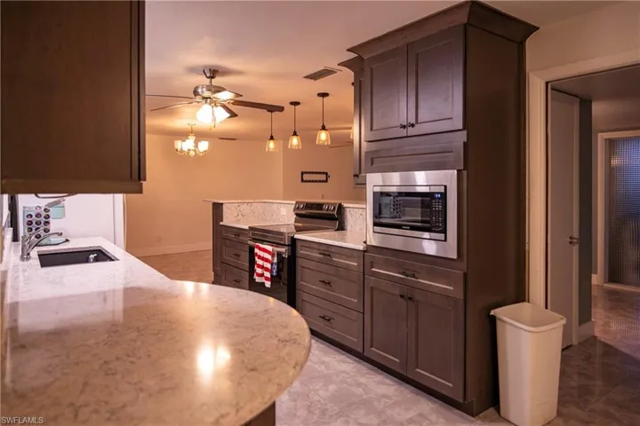 Kitchen featuring wood-finish cabinetry, stainless steel built-in microwave, stone countertops, and a double basin sink