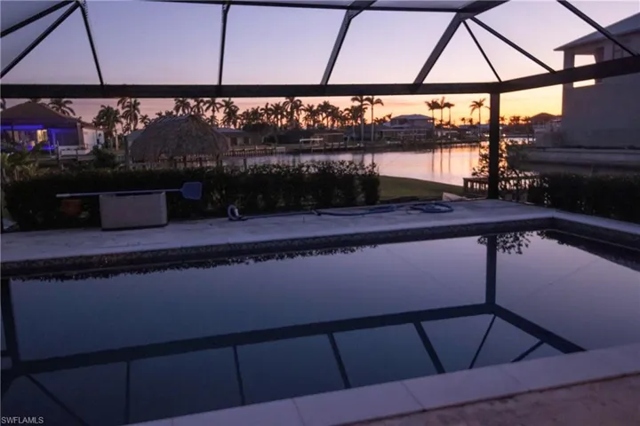 Screened swimming pool enclosure featuring a rectangular pool, concrete decking, and waterfront access
