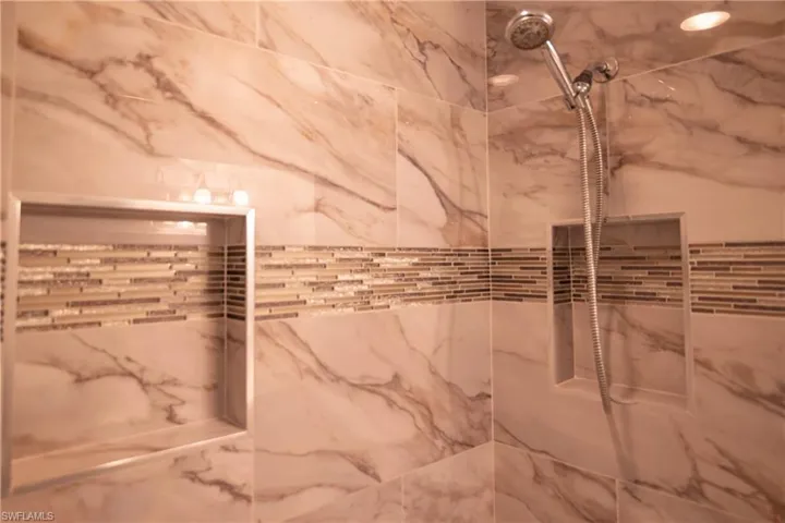 Shower stall featuring large format marbled-pattern wall tiles, a decorative mosaic tile band, and two recessed shower niches