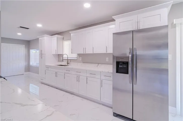 Kitchen with stainless steel refrigerator with ice dispenser, light marble finish floors, light stone counters, white cabinetry, and recessed lighting