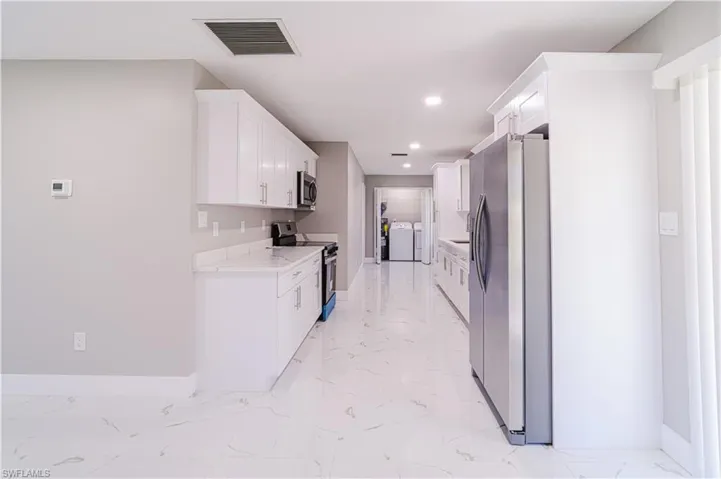 Kitchen with appliances with stainless steel finishes, white cabinets, light marble finish flooring, washer and dryer, and light stone counters