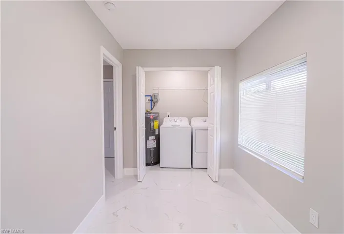 Laundry room with light marble finish floors, separate washer and dryer, and water heater