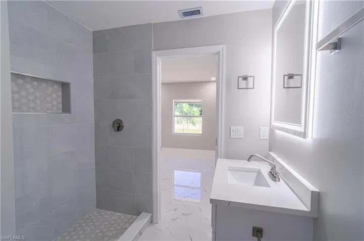 Bathroom featuring light marble finish floors, vanity, and tiled shower