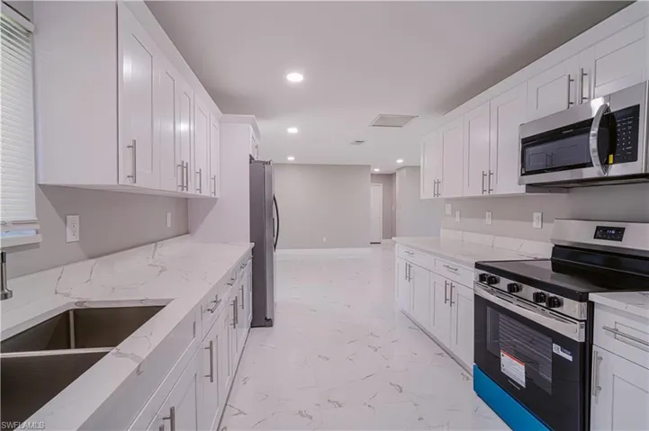 Kitchen with stainless steel appliances, white cabinets, light stone counters, and recessed lighting