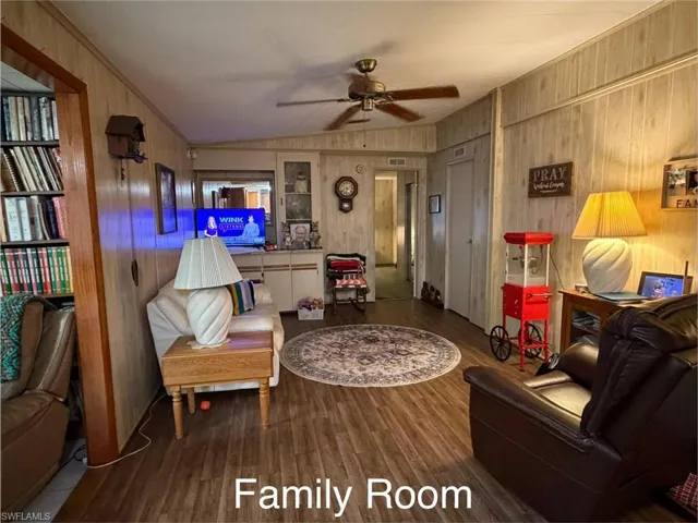 Sitting room with a ceiling fan, lofted ceiling, dark wood-type flooring, and wooden walls