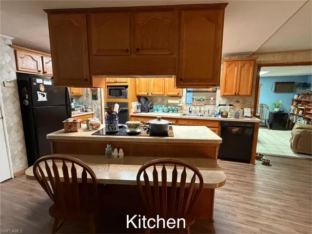 Kitchen with light countertops, black appliances, a kitchen island, and light wood-style flooring