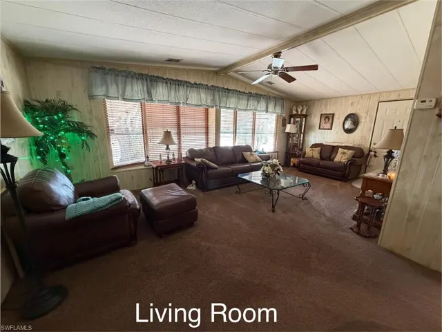 Carpeted living area featuring wood walls, a ceiling fan, and beam ceiling