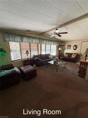 Living area featuring wooden walls, carpet floors, a ceiling fan, a textured ceiling, and beam ceiling