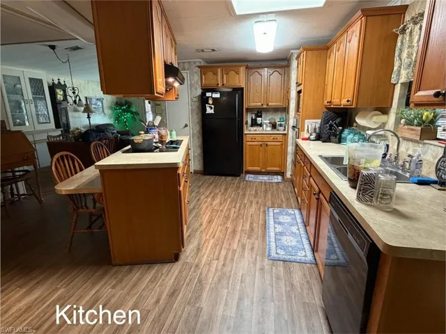 Kitchen featuring wood finish cabinets, black appliances, light countertops, a kitchen bar, and light wood-type flooring