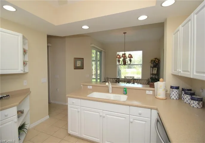Kitchen with decorative light fixtures, kitchen peninsula, sink, a chandelier, and white cabinets