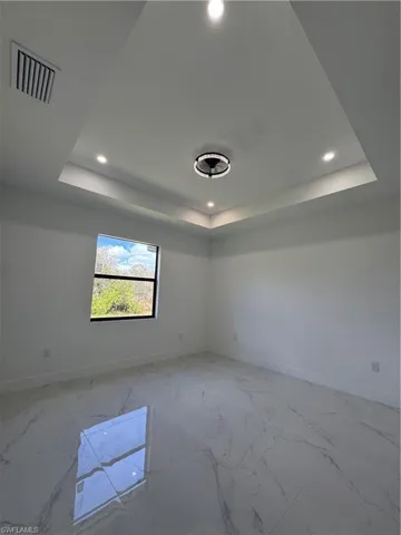 Spare room featuring recessed lighting, a tray ceiling, and light marble finish floors