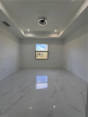 Spare room with light marble finish floors, a raised ceiling, and recessed lighting
