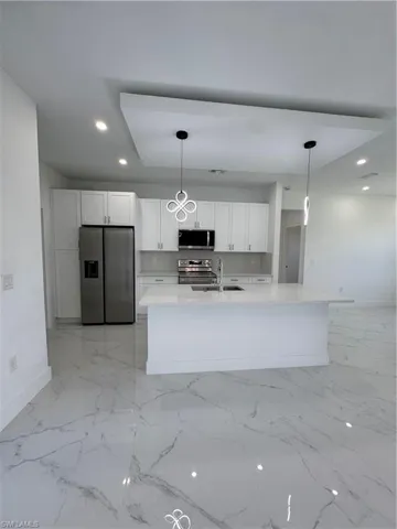 Kitchen with stainless steel appliances, white cabinets, hanging light fixtures, and light stone countertops