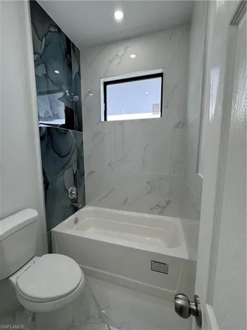 Full bath featuring marble look tiles and  shower combination