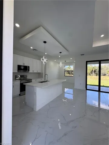 Kitchen with white cabinets, range, pendant lighting, a center island with sink, and light stone counters