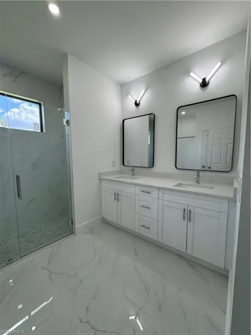 Full bathroom featuring double vanity, light marble finish flooring, a marble finish shower, and recessed lighting
