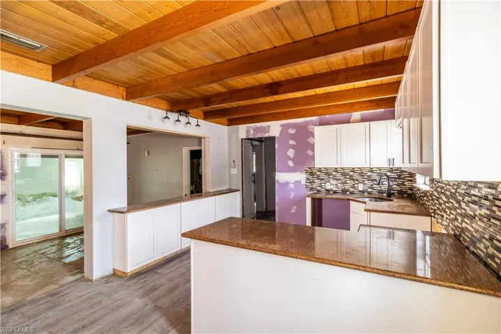 Kitchen with a wooden ceiling with exposed beams, white cabinetry, decorative backsplash, a peninsula, and dark stone counters