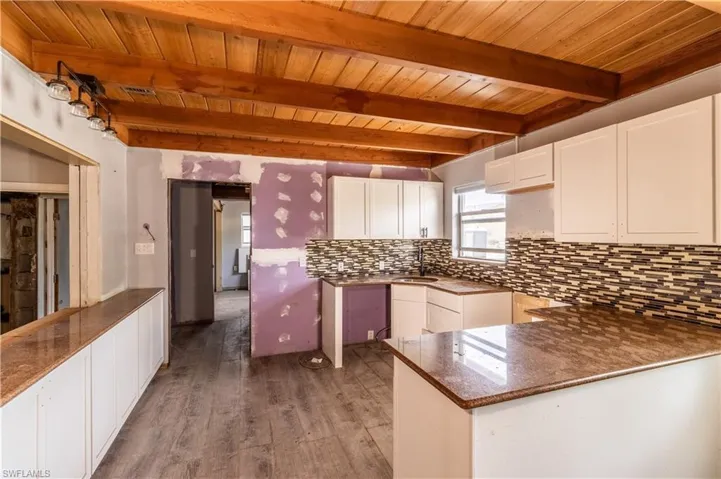Kitchen with a wooden ceiling with exposed beams, wood finished floors, tasteful backsplash, white cabinets, and a peninsula