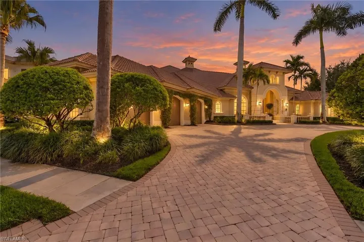 Single-story exterior featuring a paver driveway, multi-car garage, clay tile roof, and mature palm landscaping