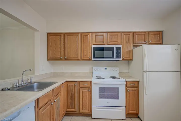 Kitchen featuring white appliances, light tile patterned flooring, light countertops, and brown cabinetry