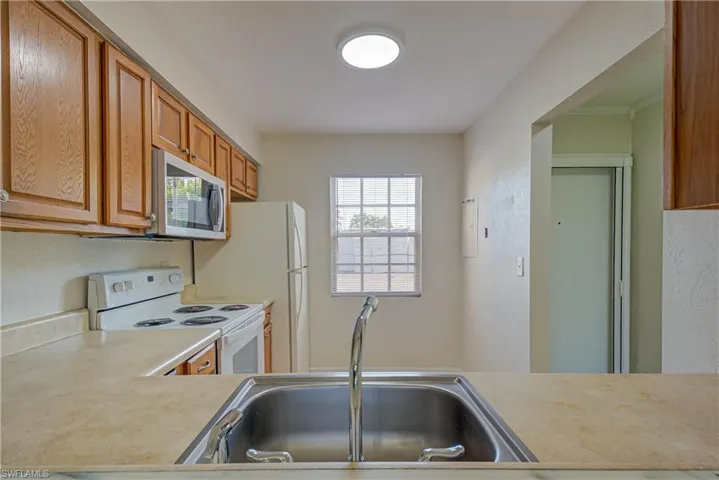 Kitchen featuring white electric range, light countertops, stainless steel microwave, and brown cabinetry