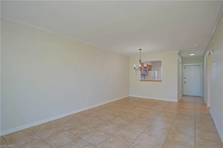 Empty room with ornamental molding, a chandelier, and light tile patterned flooring