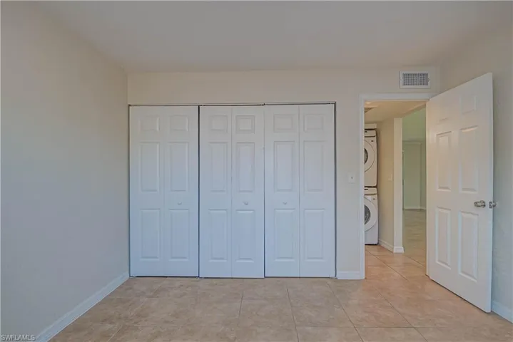 Unfurnished bedroom featuring stacked washer / dryer, light tile patterned flooring, and a closet