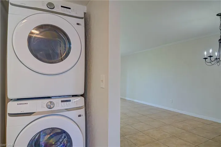 Washroom featuring stacked washer / dryer, ornamental molding, a chandelier, and light tile patterned floors