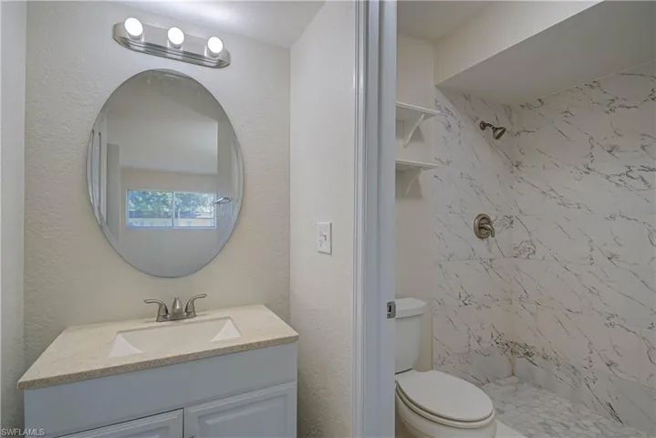 Bathroom with vanity, a tile shower, and a textured wall