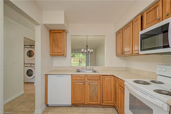 Kitchen featuring white appliances, stacked washer / drying machine, a chandelier, and light tile patterned floors
