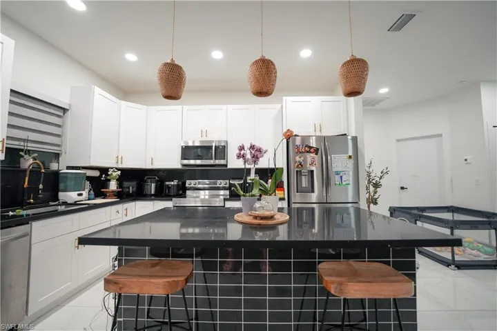 Kitchen featuring recessed lighting, a kitchen bar, light marble finish floors, stainless steel appliances, and white cabinetry