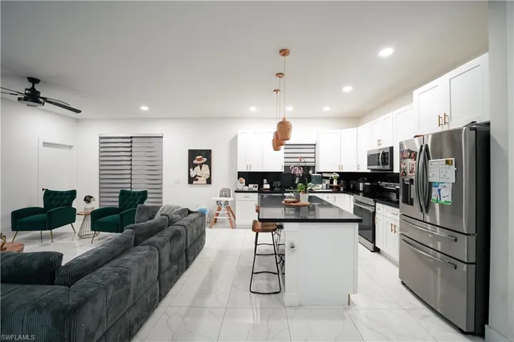 Kitchen featuring open floor plan, stainless steel appliances, dark countertops, a breakfast bar, and light marble finish floors