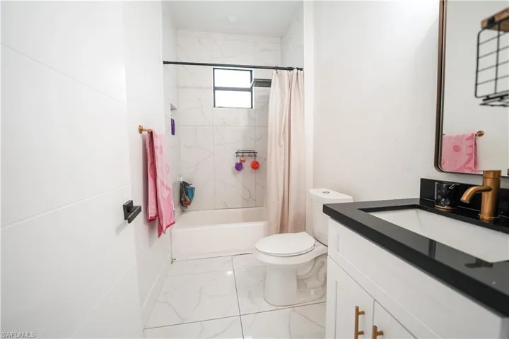 Bathroom featuring marble look tiles, vanity, and shower / tub combo with curtain