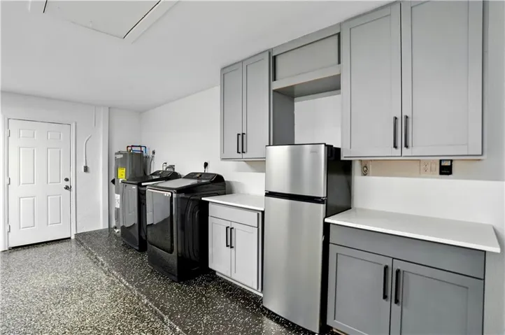 Garage featuring gray cabinetry, freestanding refrigerator, open shelves, independent washer and dryer, and electric water heater