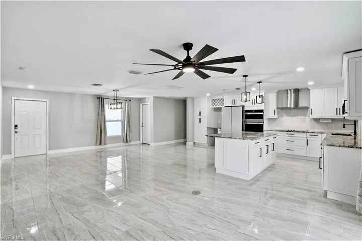 Kitchen with tasteful backsplash, white cabinets, recessed lighting, light stone countertops, and a kitchen island
