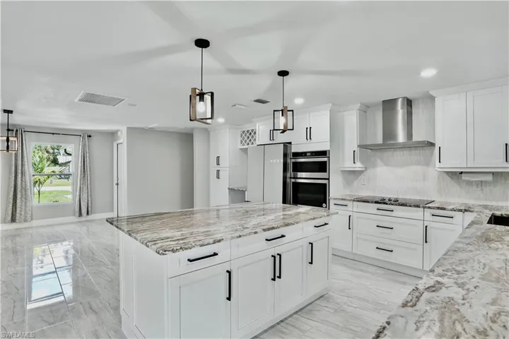 Kitchen featuring backsplash, light stone counters, a center island, pendant lighting, and wall chimney range hood