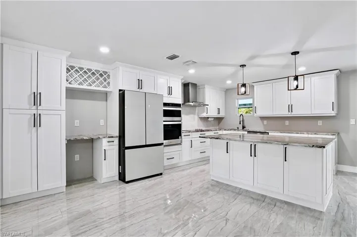 Kitchen with freestanding refrigerator, light stone countertops, pendant lighting, a center island, and wall chimney range hood