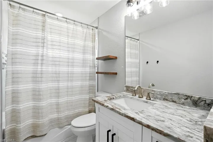 Full bathroom featuring shower / tub combo with curtain, a textured wall, and vanity