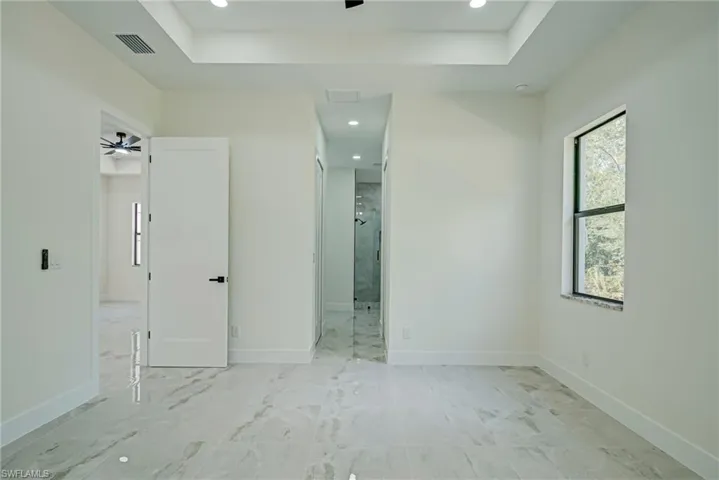 Unfurnished bedroom featuring a raised ceiling, recessed lighting, ensuite bath, and light marble finish floors