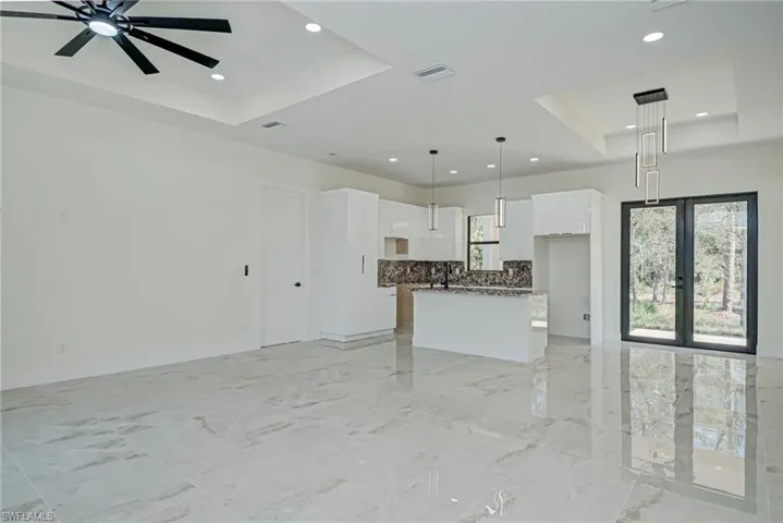 Unfurnished living room with a raised ceiling, light marble finish flooring, recessed lighting, ceiling fan, and french doors