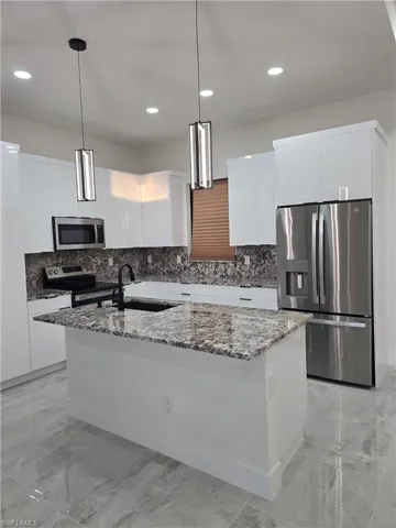Kitchen with dark stone countertops, white cabinets, appliances with stainless steel finishes, pendant lighting, and recessed lighting