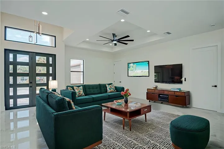 Living room with a tray ceiling, recessed lighting, french doors, and a ceiling fan