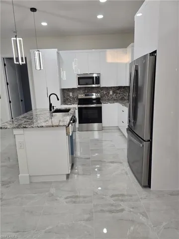 Kitchen featuring modern cabinets, stainless steel appliances, white cabinets, light stone counters, and a kitchen island with sink