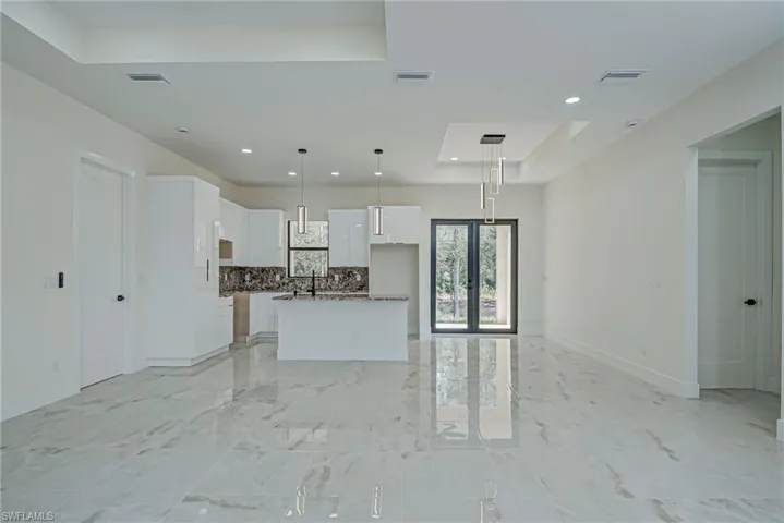 Kitchen featuring a tray ceiling, backsplash, light marble finish flooring, a center island with sink, and white cabinetry