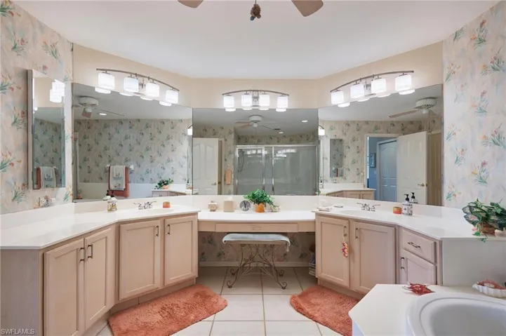 Full bath featuring two vanities, a shower stall, light tile patterned floors, ceiling fan, and wallpapered walls