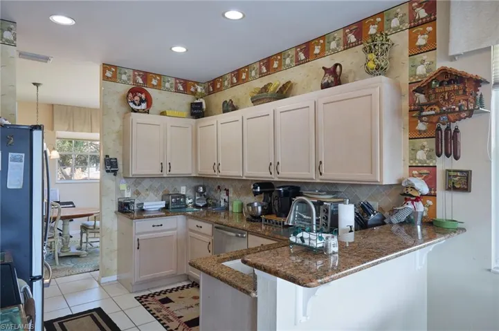 Kitchen featuring wallpapered walls, a peninsula, dark stone counters, stainless steel appliances, and backsplash